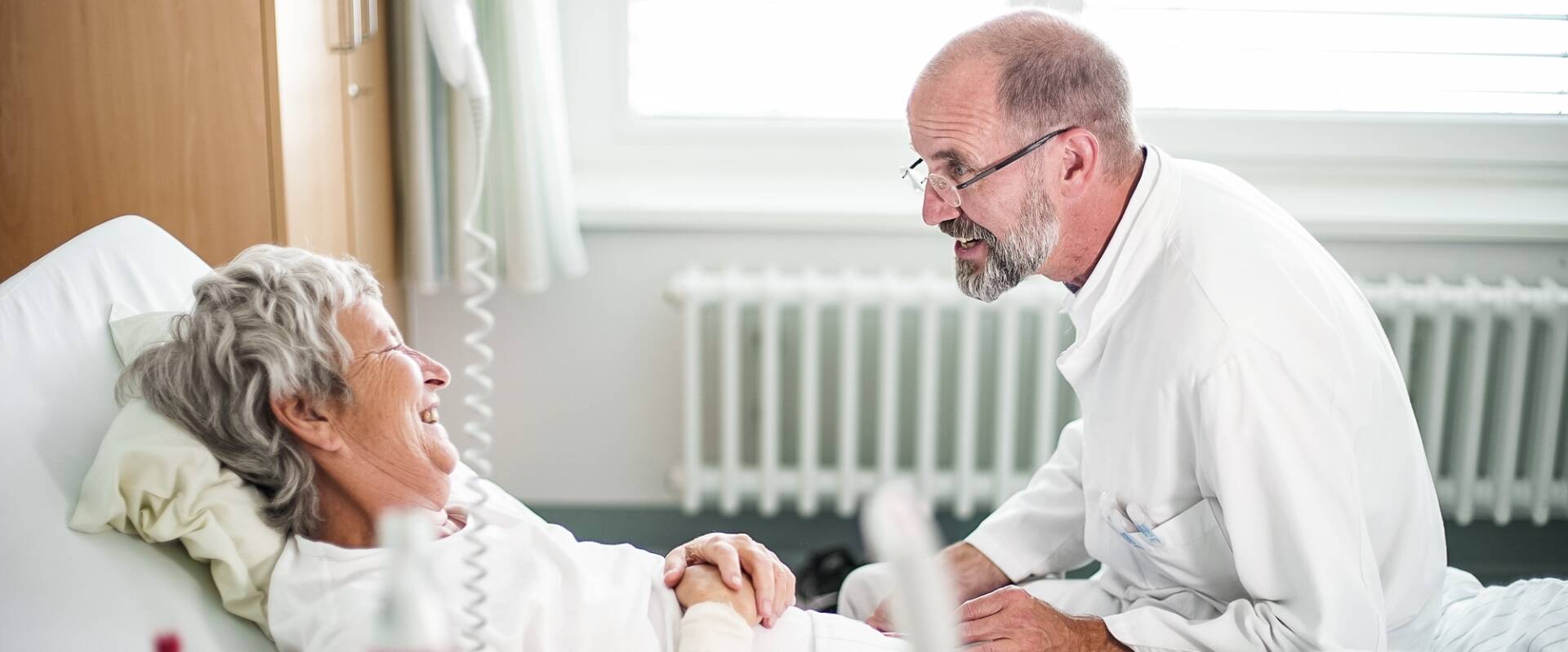 Arzt sitzt am Bett einer Patientin und gibt ihre Diagnose ab
